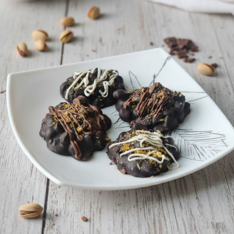 Chocolate cookies with decorative elements on a white plate with scattered nuts and chocolate pieces on a wooden surface.