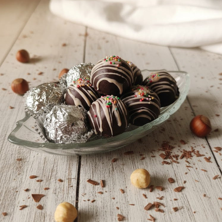 Chocolate truffles on a glass plate with nuts and cocoa on a wooden surface