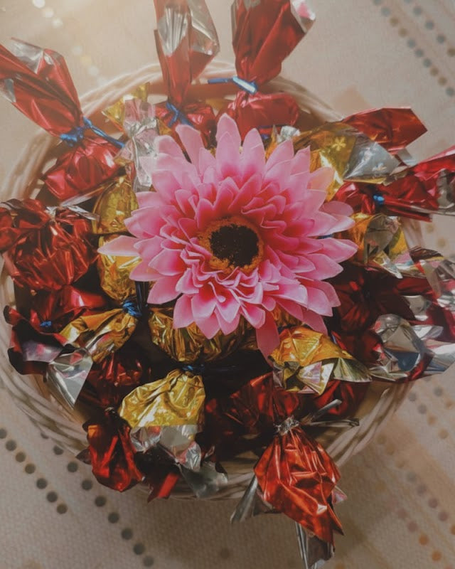 Pink flower surrounded by wrapped candies on a textured surface