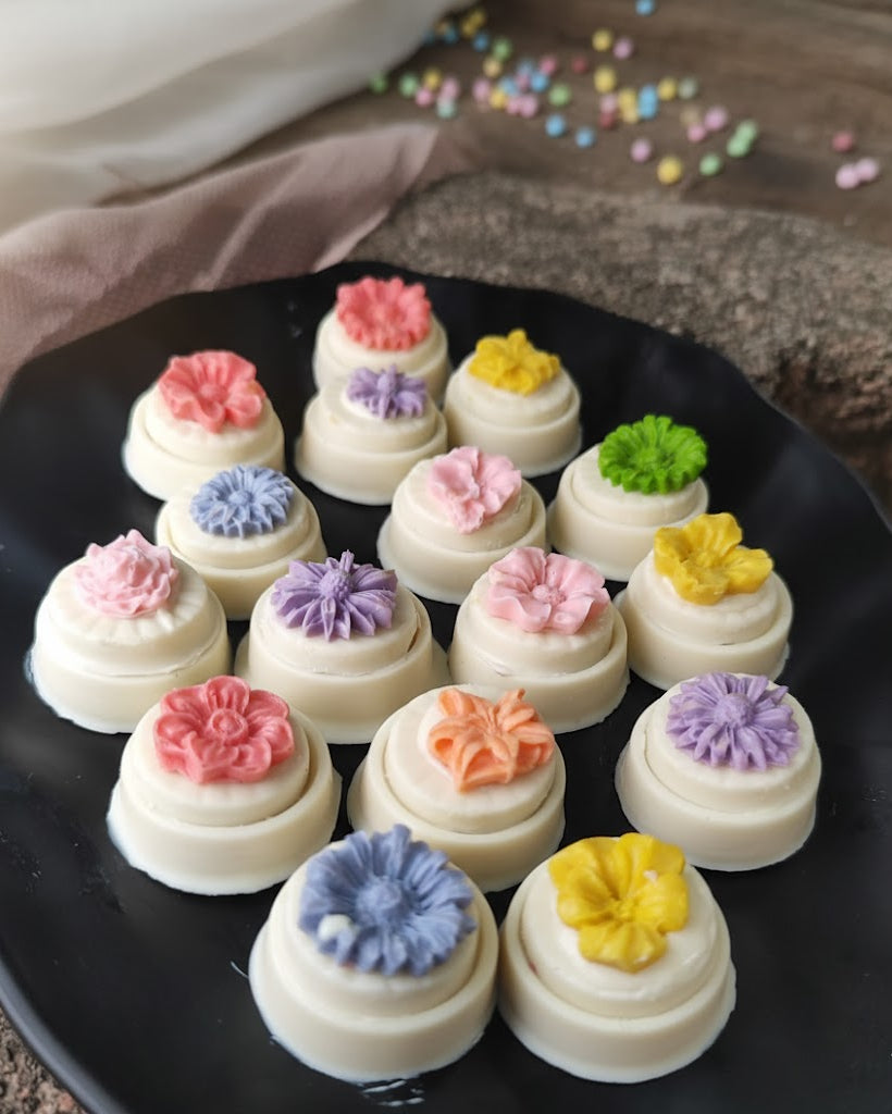 Small decorated cakes with colorful icing on a black plate.