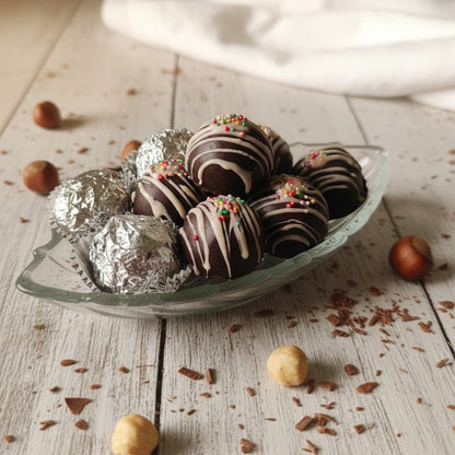 Chocolate truffles on a glass plate with nuts and cocoa on a wooden surface