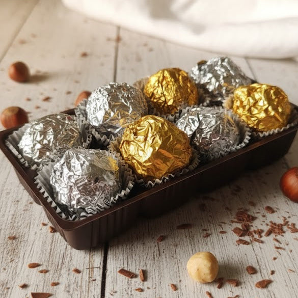 Assorted chocolate truffles in silver and gold foil on a wooden surface with nuts.