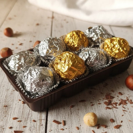 Assorted chocolate truffles in silver and gold foil on a wooden surface with nuts.