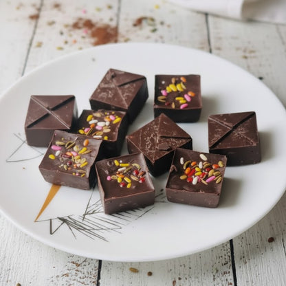 Chocolate squares with sprinkles on a white plate on a wooden surface